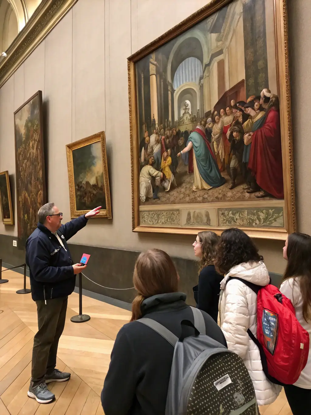 A photograph of a guided tour group listening to a curator discuss Van Gogh's 'The Potato Eaters' at the Van Gogh Museum.